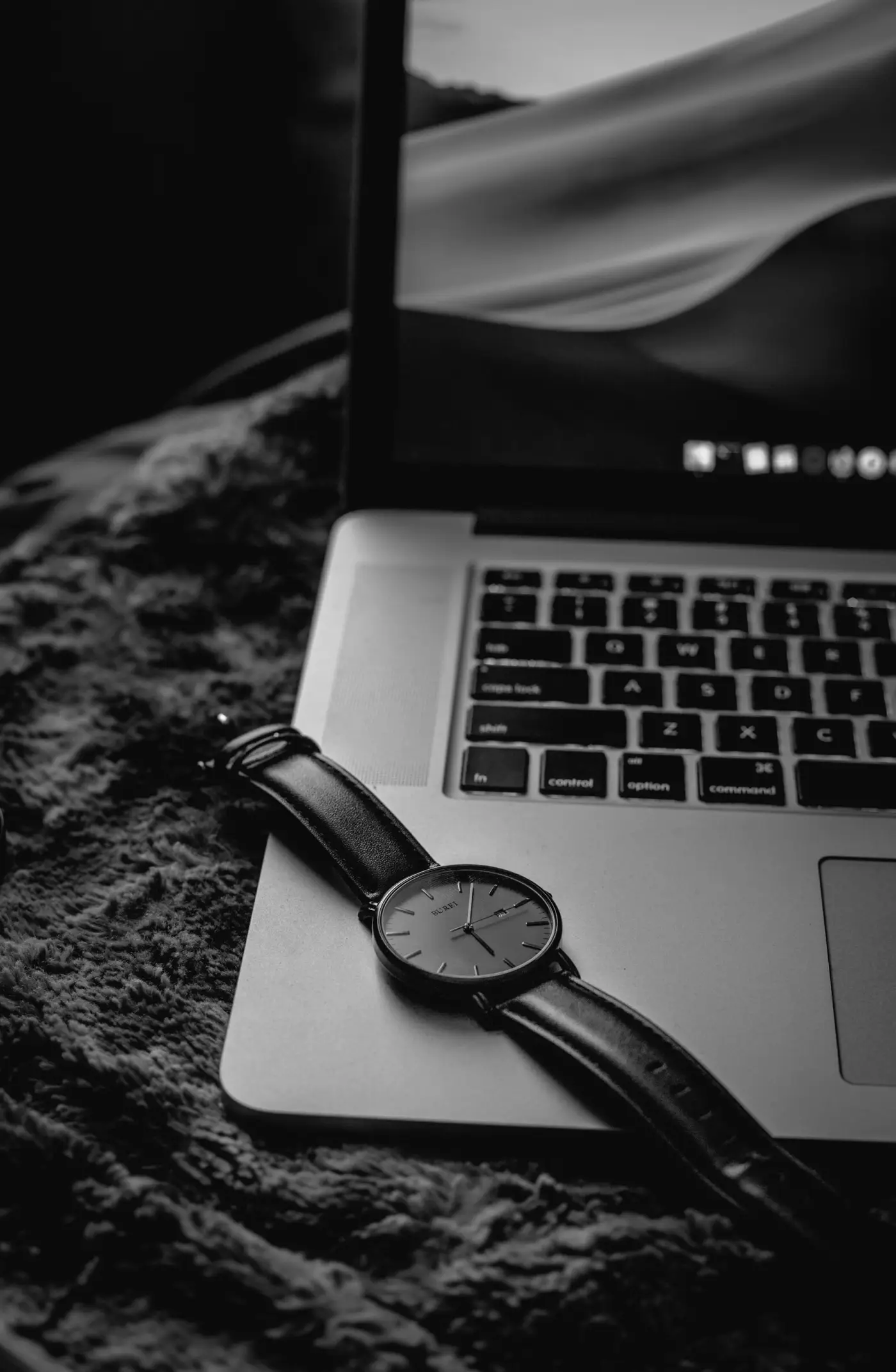 A laptop and a wristwatch on a dark desk